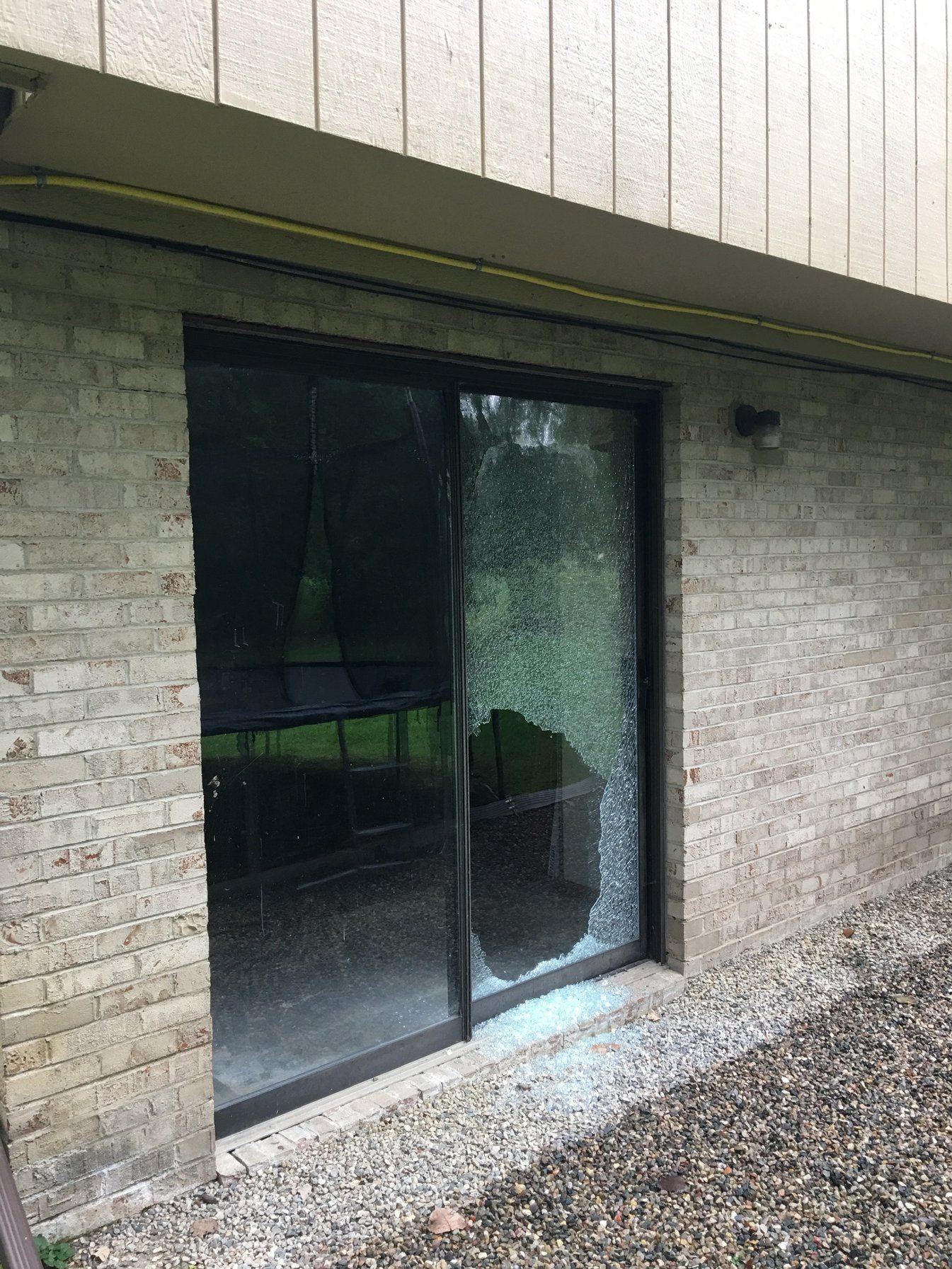 Old dark sliding patio door with a shattered glass panel in a light brick wall
